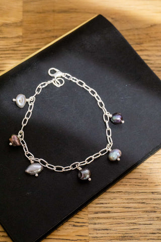 Silver-tone charm bracelet with multiple dangling bead charms on a black display card