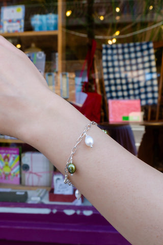 Silver-tone bracelet with pearl centerpiece and green dangling charm on wrist