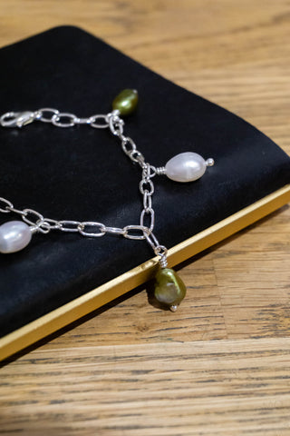 Silver-tone bracelet detail with pearl and green bead charms and curved links