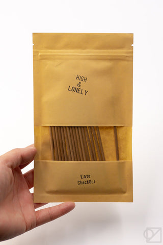 Golden incense pouch with front logo and window showing incense sticks, held in hand