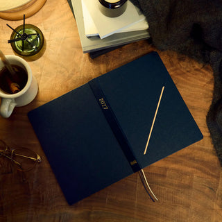A5 slash planner opened showing 2027 on the spine with gold diagonal line and ribbons