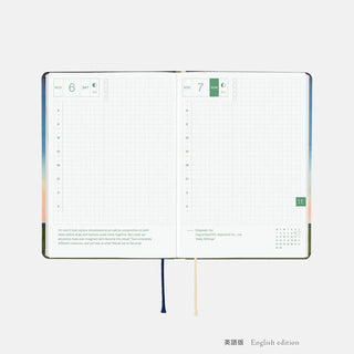 A6 planner open to weekly grid pages with small green and orange markers