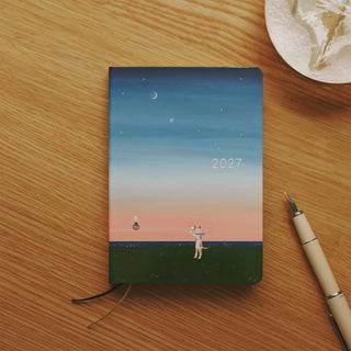 A6 planner on desk with blue sky and 2027 sunset illustration