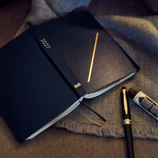 Hobonichi HON A6 slash planner on angle, navy cover with gold diagonal stripe and 2027