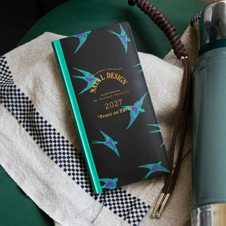 2027 weeks planner on table with dark cover, teal edge, and teal bird pattern.