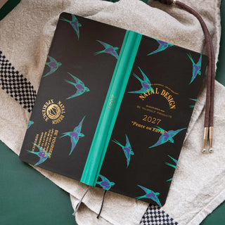 2027 weeks planner laid open with dark covers, teal spine, and teal bird print.
