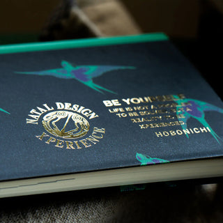 Close-up of planner cover with gold and teal logo text and small bird motifs.