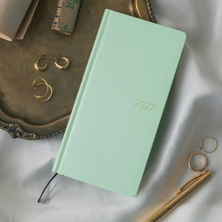 Angled jade green 2027 WEEKS planner cover with gold “2027” and black ties