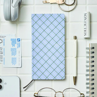 Plaid planner notebook cover with two black elastic ties on a white desk surface