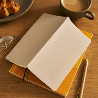 Hobonichi Techo WEEKS planner with smooth café au lait cover, open on orange notebook