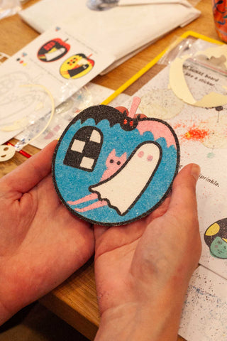 Hand holding a blue and black patch with a penguin character design