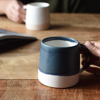 Navy and white ceramic mug held by hand, wide rim and curved handle