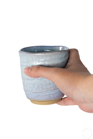 Light blue textured ceramic teacup held in hand, brown foot base