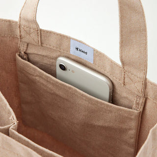 Beige canvas tool tote close-up with side pocket holding a smartphone; brand label.