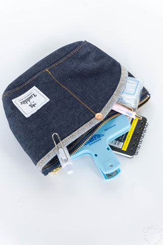 Small dark denim pouch with gold zipper and front label, open with notebook inside
