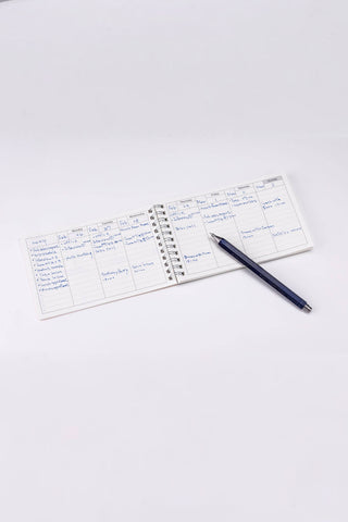 Weekly schedule planner open with pen, showing writing areas across days