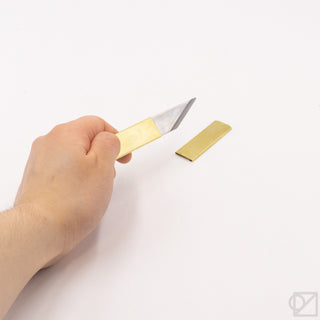 Small brass knife held by hand, with exposed silver blade and brass sheath
