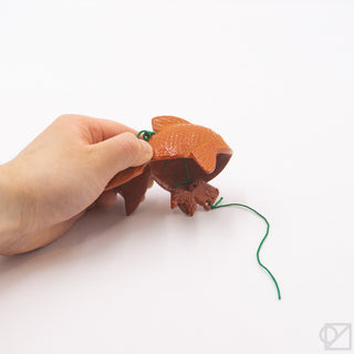 Orange fish wind chime held by hand, green cords and hanging loop visible