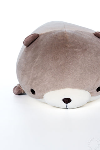 Small otter hugging pillow plush close-up, taupe-gray face with white muzzle and dark nose