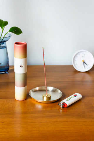 Gradient incense tube with gold logo; incense stick in brass holder on tray