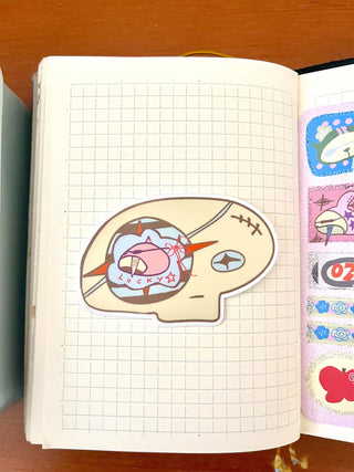 Skull-shaped vinyl sticker with pink character, orange stars, and blue details
