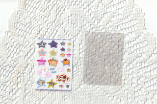 Small clear sticker sheet with colorful cartoon icons on white textured fabric