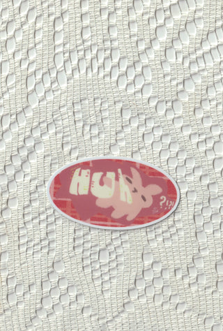 Oval nonalouie vinyl sticker on white textured surface, pink with “Huh?!” text