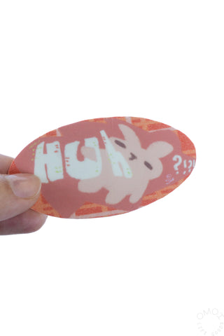Oval nonalouie vinyl sticker held in hand, pink with white “Huh?!”