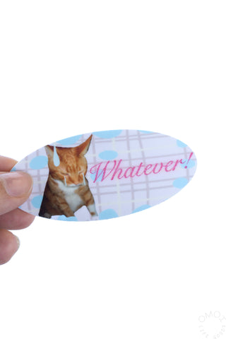 Vinyl sticker held by finger, orange cat with 'Whatever!' pink script