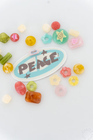 Peace! oval sticker with turquoise center, surrounded by small colorful charms