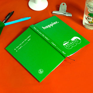 Green diary notebook with "happier." title and small face illustration on cover