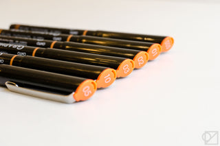 Black pens with orange end caps, laid diagonally; close view of pen tips