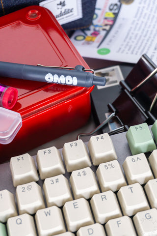 Blue OMOI logo gel pen placed among keyboard keys