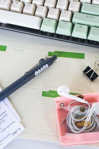 Blue gel pen lying across weekly planner page near pink pencil accessories case