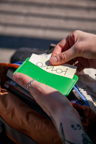 Slim green card slip wallet held in hand, with embossed branding on the front