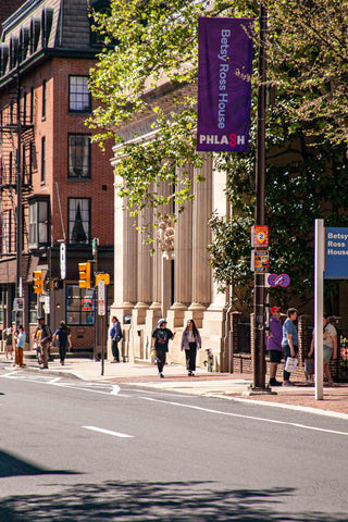 A & J walk up Arch street near the Betsy Ross House. Our view is from across the street of them. They pass historical buildings of various architectural styles. 