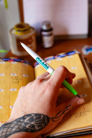 OMOI Shop Pen key lime green pen held in a hand above an open notebook