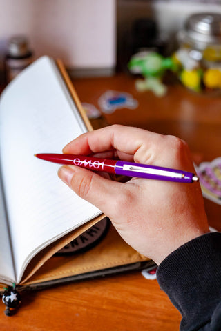 OMOI Shop Pen dark berry pen held over an open notebook