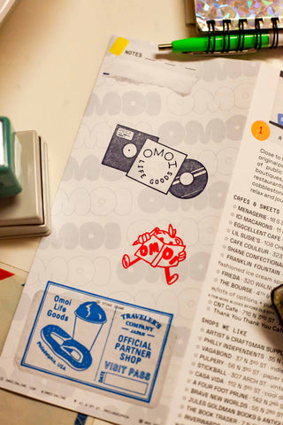 OMOI's short trips guidebook open with logo stickers and partner shop stamp area.