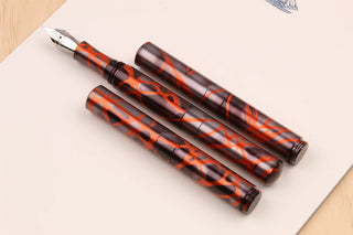 Two orange smoke marbled fountain pens with metal nibs on paper