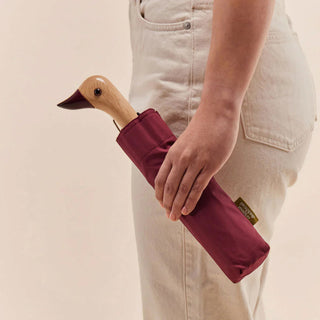 Duck umbrella with maroon compact case held in hand; duck-shaped wooden grip