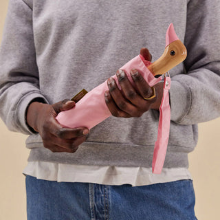 Compact duck umbrella in powder pink, held open by a person in a gray sweatshirt