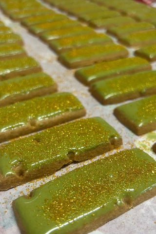 Green matcha lemon shortbread bars on parchment with sparkling golden bits