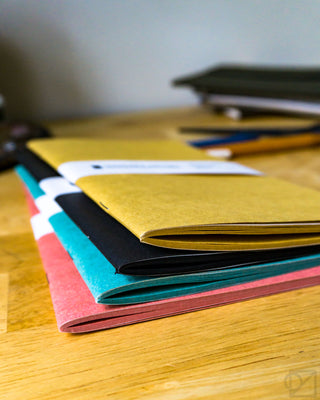 Assorted kraft notebook refills in yellow, blue, teal, and pink stacks