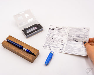 Fountain pen maintenance kit with blue pen, wooden block, and instruction sheet