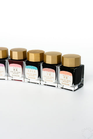 Bottled ink set lineup of clear square bottles with gold caps and colored labels