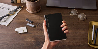 Hand holding a black slim notebook with yellow label band on the cover