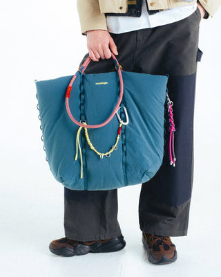 Teal and pink braided keychain with metal clip, hanging on a tote bag handle