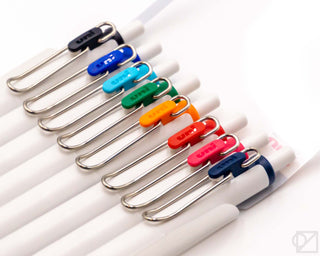 Eight Uni-Ball One 0.38mm gel pens with white barrels, colored clips, and tips, angled view