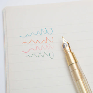 Gold brass dip pen beside notebook page with colorful wave practice strokes